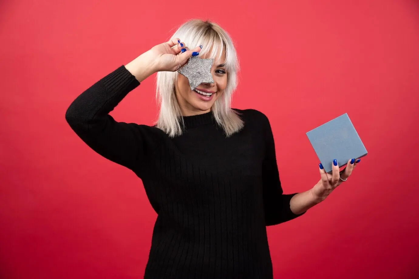 Молодая женщина держит подарок со звездой на фоне красной стены.